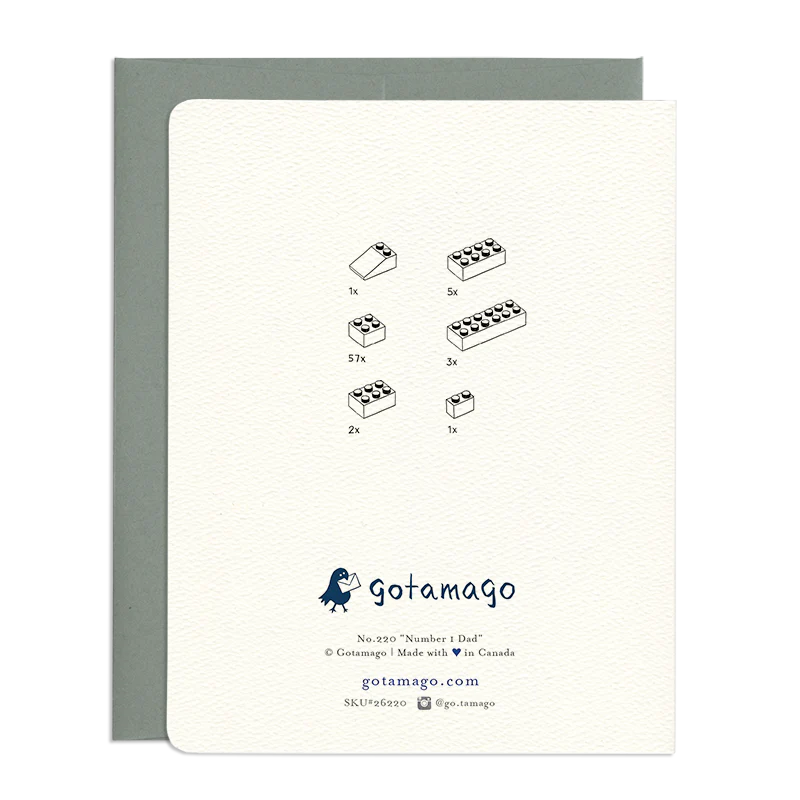 The card displays a minimalist design featuring a collection of building block illustrations. Each illustration is accompanied by a number indicating the quantity of that particular block. Below the illustrations, the brand "gotamago" is prominently displayed with a small bird logo. Further details include the product number "No. 220 'Number 1 Dad'", copyright information, website address, and social media handle. The card itself has a textured, off-white finish and is presented within a light grey envelope