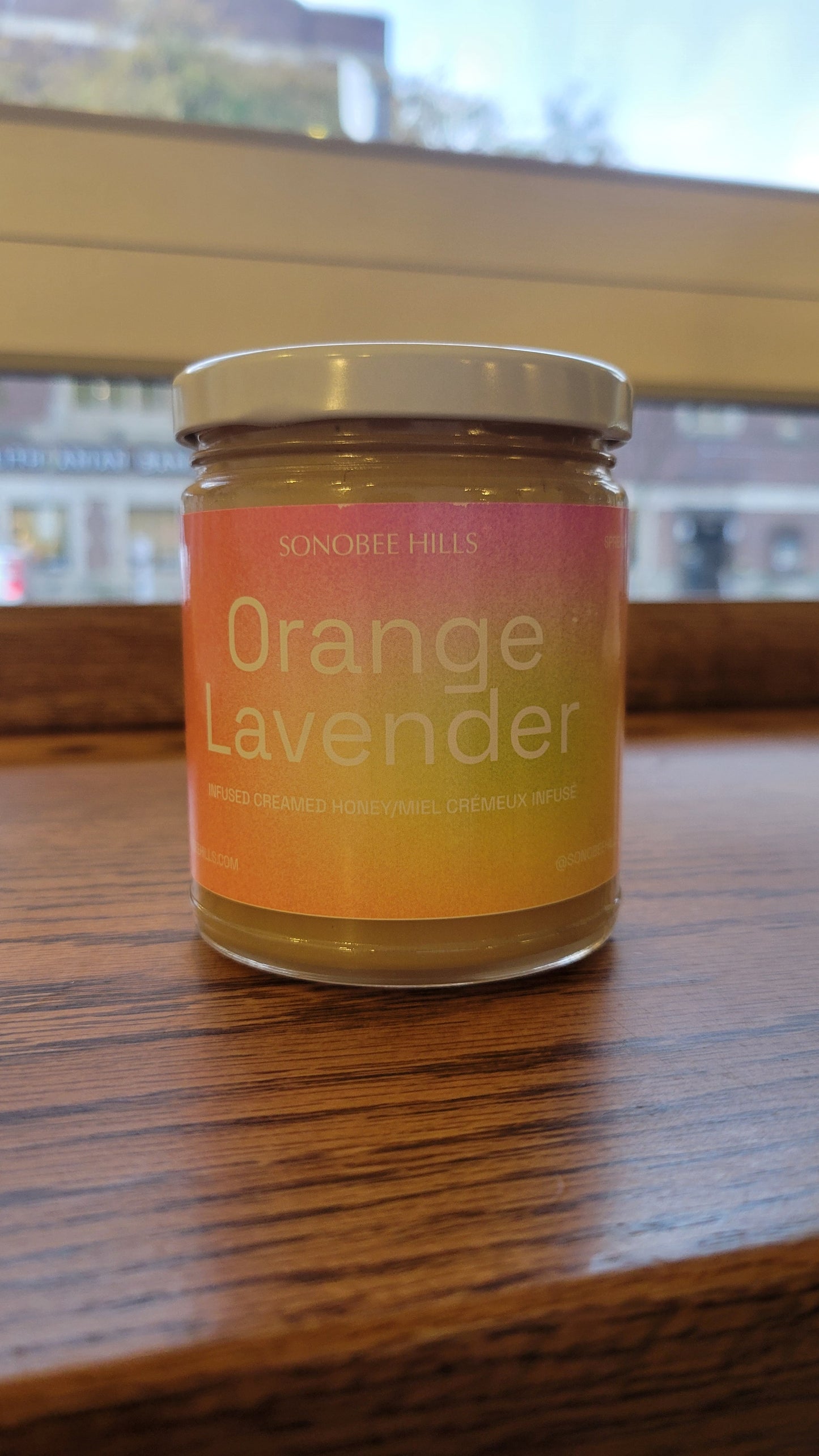 Jar of 'Orange Lavender' honey on a wooden surface with a blurred background